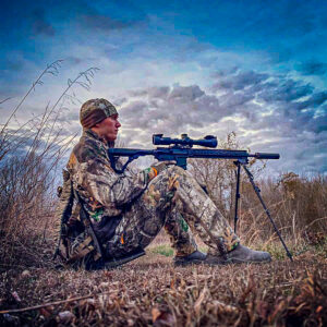 hunter sitting in exoskeleton frame pack shooting rifle